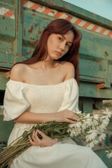 Thoughtful young woman with daisies sitting by farm trailer.Retro grain effect