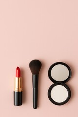 Cosmetic products for makeup red lipstick, powder and brush on vertical pink background with copy space.