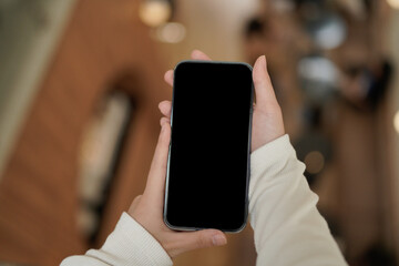 Mockup of a hand holding mobile phone with blank white screen in cafe