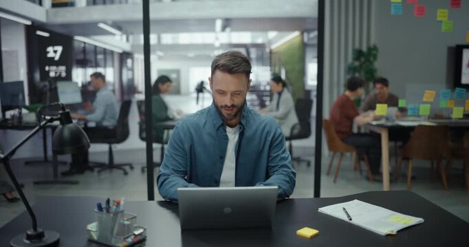 Successful Art Director Working on Laptop Computer in Big Business Office with Diverse Colleagues in the Background. Businessman Preparing for a Marketing Plan Meeting Discussion with Board Members