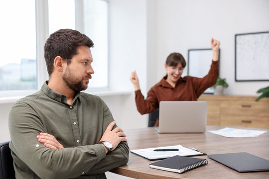 Man feeling jealous of his colleague's success in office, selective focus