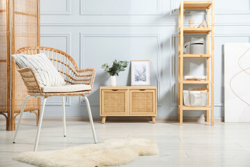 Stylish armchair with pillow, cabinet and decor indoors. Interior design