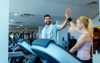 Man and woman running on treadmill at gym giving hi five to each other.