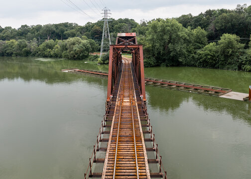 Aerial view of a rusty railroad trestle swing bridge cutting across the Fox River, its aged metal contrasting with the lush green trees lining the banks. Appleton, Wisconsin, United States.