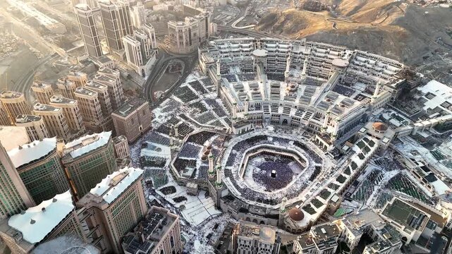 drone footage of Mecca, Saudi Arabia, filmed at sunset. The video captures the vast urban landscape with residential buildings, modern towers, and surrounding mountains bathed in golden hour light