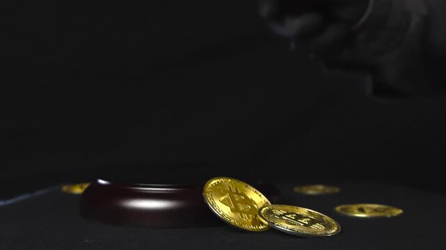 Close up slow motion footage of a justice court brown wooden hammer with bronze decoration slamming down and golden shiny and reflective bitcoin cryptocurrency coins around it flying and bouncing.