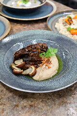 Close-up view of a gourmet restaurant dish, braised beef cheeks served with creamy mashed potatoes and mushrooms, rustic presentation on a stylish plate.