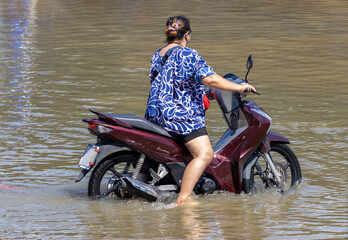 A woman tries to ride a motorbike through a flooded street, Thailand
