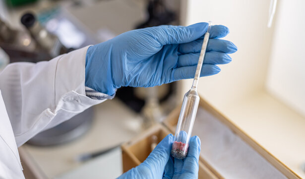 A female chemist takes a hydrometer to subsequently measure the density of a liquid by immersing the hydrometer and recording the result on a scale