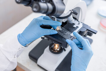 Female scientist using microscope in laboratory. Biotechnology specialist looking under microscope, doing analysis of test sample. Medical science laboratory: advanced equipment.