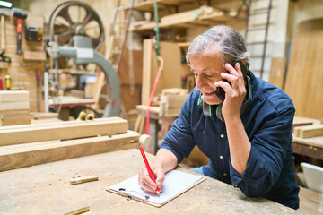 Experienced craftsman talking on phone in a busy wood workshop