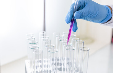 Scientist dripping color liquid into test tube in laboratory. Pipette with a drop and scientific laboratory test tubes in a research laboratory. Medical science laboratory glassware.