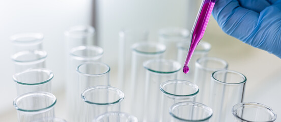 Scientist dripping color liquid into test tube in laboratory. Pipette with a drop and scientific laboratory test tubes in a research laboratory. Medical science laboratory glassware.