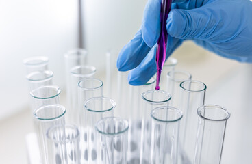 Scientist dripping color liquid into test tube in laboratory. Pipette with a drop and scientific laboratory test tubes in a research laboratory. Medical science laboratory glassware.