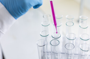 Scientist dripping color liquid into test tube in laboratory. Pipette with a drop and scientific laboratory test tubes in a research laboratory. Medical science laboratory glassware.