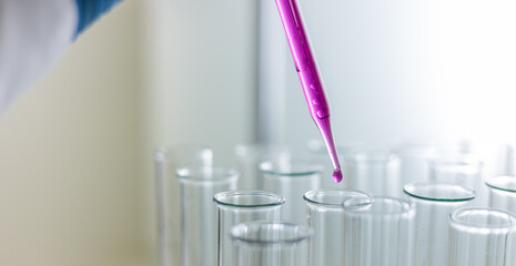 Scientist dripping color liquid into test tube in laboratory. Pipette with a drop and scientific laboratory test tubes in a research laboratory. Medical science laboratory glassware.