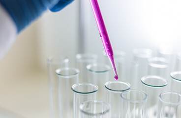 Scientist dripping color liquid into test tube in laboratory. Pipette with a drop and scientific laboratory test tubes in a research laboratory. Medical science laboratory glassware.