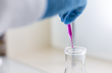 Chemist carries out analysis of water with chemical reagents. Female scientist dripping liquid from pipette into flask in laboratory.