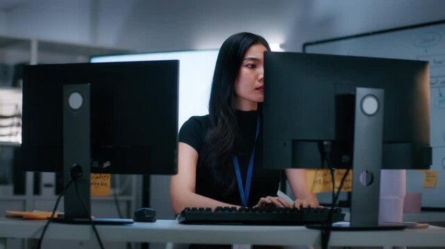 Asian Female Software Engineer Working on new innovation business startup project, Focused on Developing software, Writing code with Dual monitor screens sitting at desk in software tech office.