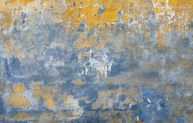 Old grunge wall surface with cracked paint in blue and yellow tones, weathered vintage background.