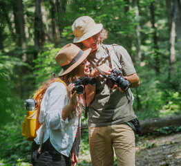 Young happy couple hiking in summer forest with camera and binocular