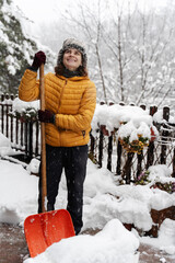 Woman cleaning snow from porch near her cottage and using snow shovel. Winter season
