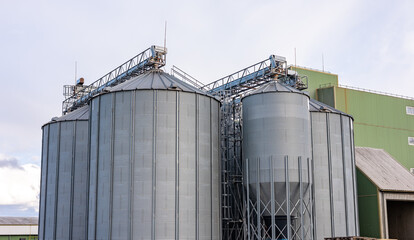 A low-angle view of large fly ash silos at an industrial plant, showcasing the towering infrastructure used for ash storage and processing. The silos are equipped with ladders and metal support struct