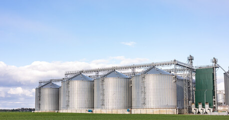 Plant for processing and silos for drying cleaning and storage of agricultural products, flour, cereals and grain. Silver tanks close-up. Silos in a barley field. Storage of the crop