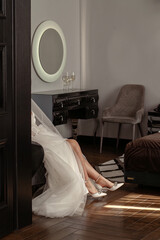 Cropped image of bride putting on high heeled shoes in bedroom