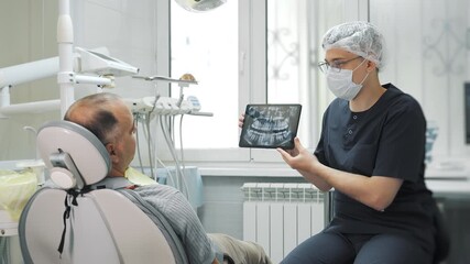 A dentist shows a patient an X-ray of their jaw on a tablet. A patient consultation at a modern dental clinic. - Powered by Adobe