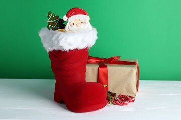 Happy Saint Nicholas day. Red boot with sweets and gift box on white wooden table against green background