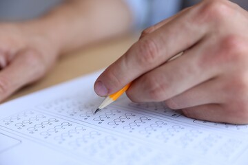 Student filling out multiple choice test at table, closeup. Passing exam
