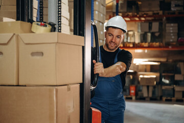 Preparing boxes for shipment by moving them by forklift. Man in uniform is working in the storage