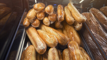 Bread showcase in market with wheat baguettes wrapped in plastic.