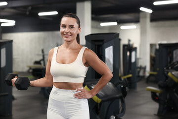 Fototapeta premium Smiling woman training with dumbbell in gym. Space for text
