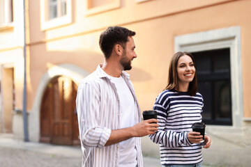 Coffee to go. Couple with paper cups of drinks walking on city street, space for text