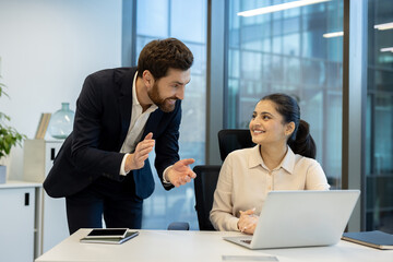 Experienced businessman actively mentoring a young female colleague at her desk, discussing project details and fostering professional growth in a modern office environment