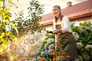 Senior woman watering beautiful flowers with hose in garden