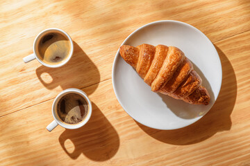 Two espresso cups and croissant in morning sun rays