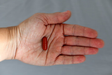 A top-down shot of an open palm holding a single, dark red capsule, set against a plain gray background for a clean, medical-themed image.