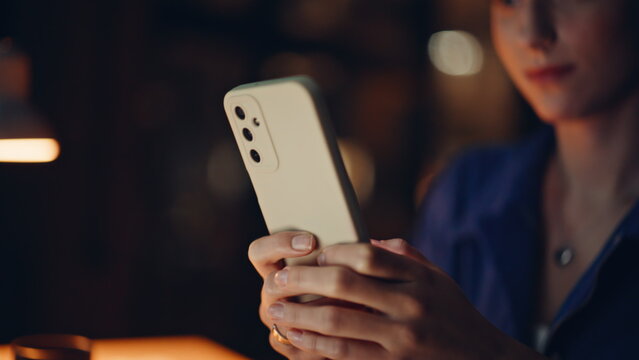 Cheerful brunette messaging smartphone at night home closeup. Happy woman sms