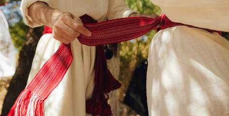 Close-up of Ukrainian traditional costume embroidered vyshyvanka blouse, woven belt kraika, folk jewelry. Ethnic festive clothing, national outfit details, cultural heritage. Part of the series
