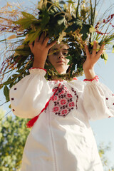 Close-up of Ukrainian girl in traditional blouse Vyshyvanka weaving a flower wreath for Ivana Kupala celebration. Folk costume, midsummer Slavic holiday, cultural tradition. Part of the series
