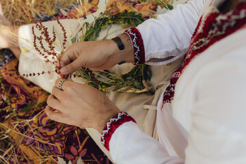 Close-up of hand in Ukrainian traditional blouse Vyshyvanka weaving a flower wreath for Ivana Kupala celebration. Folk costume, midsummer Slavic holiday, cultural tradition. Part of the series