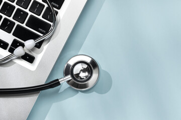 Stethoscope and laptop on soft blue background, illustrating blend of healthcare and digital...