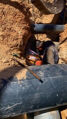 Male welder works. Welding joint of large diameter pipe. in Rural Landscape: A new metal pipe lies in a rocky ditch, with sand hills and distant mountains providing a scenic backdrop.
