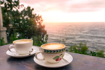 Two cappuccino latte macchiato cups on terrace at seaside sunset with ocean view, relaxing moment