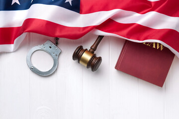 Judge's gavel, handcuffs and law book with American flag on a white wooden desk.
