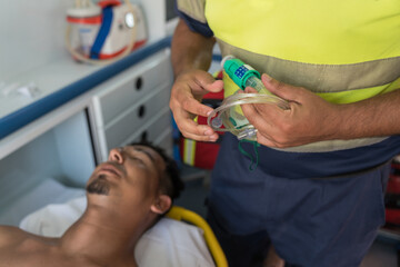 Paramedic preparing oxygen mask for patient lying on stretcher inside ambulance