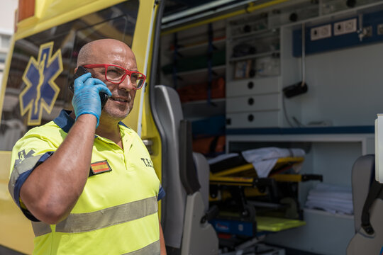 Paramedic wearing protective gloves talking on phone near ambulance